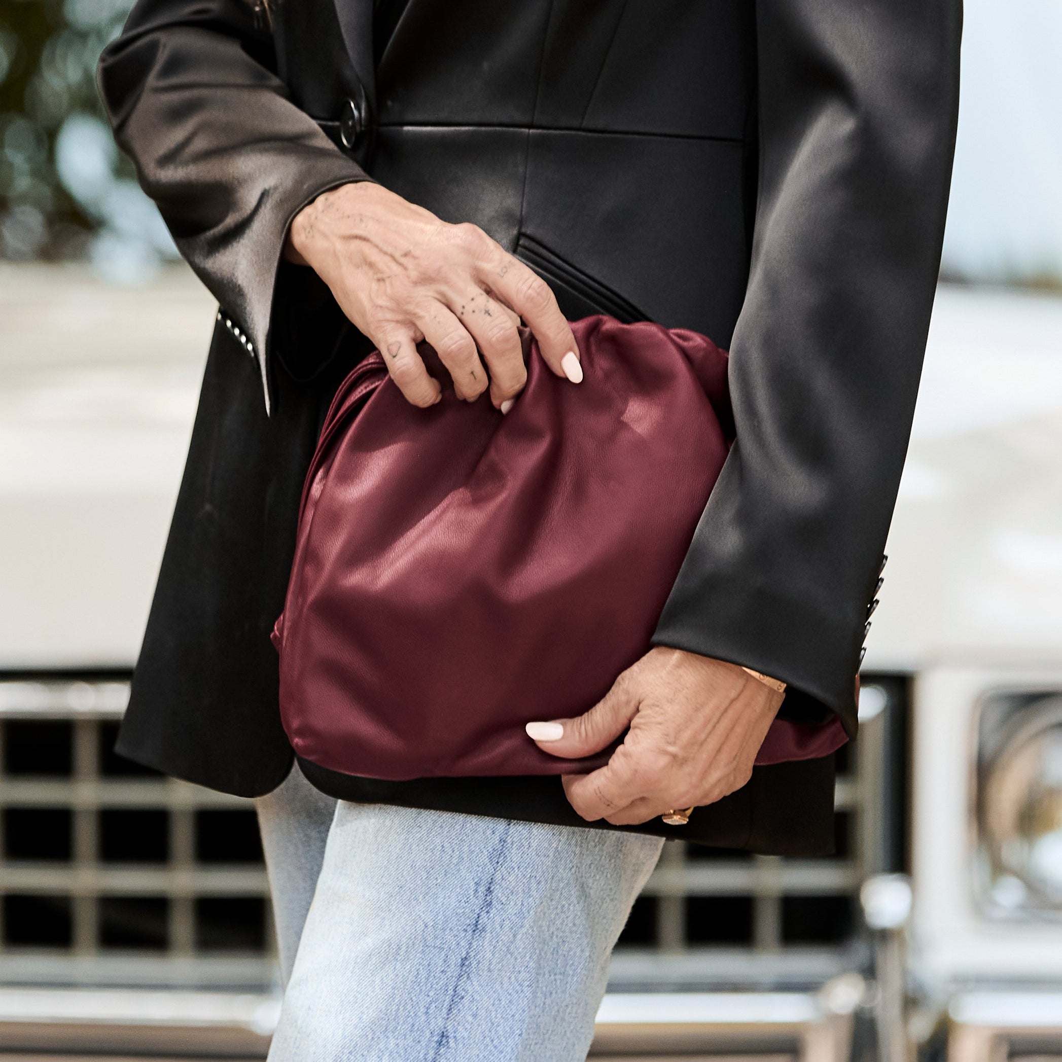 Tish Cyrus holding a maroon clutch bag with a blurred background